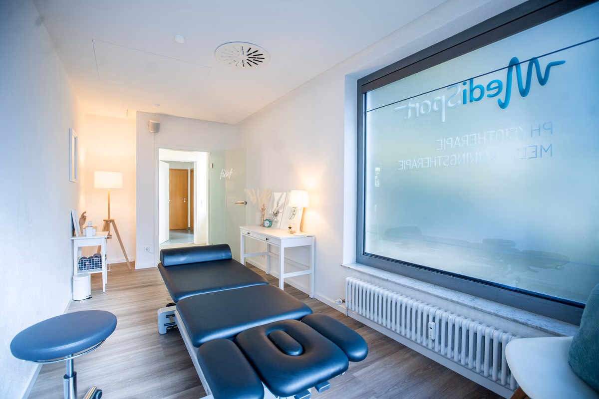 Behandlungsraum mit Therapieliege und MediSport-Logo am Fenster